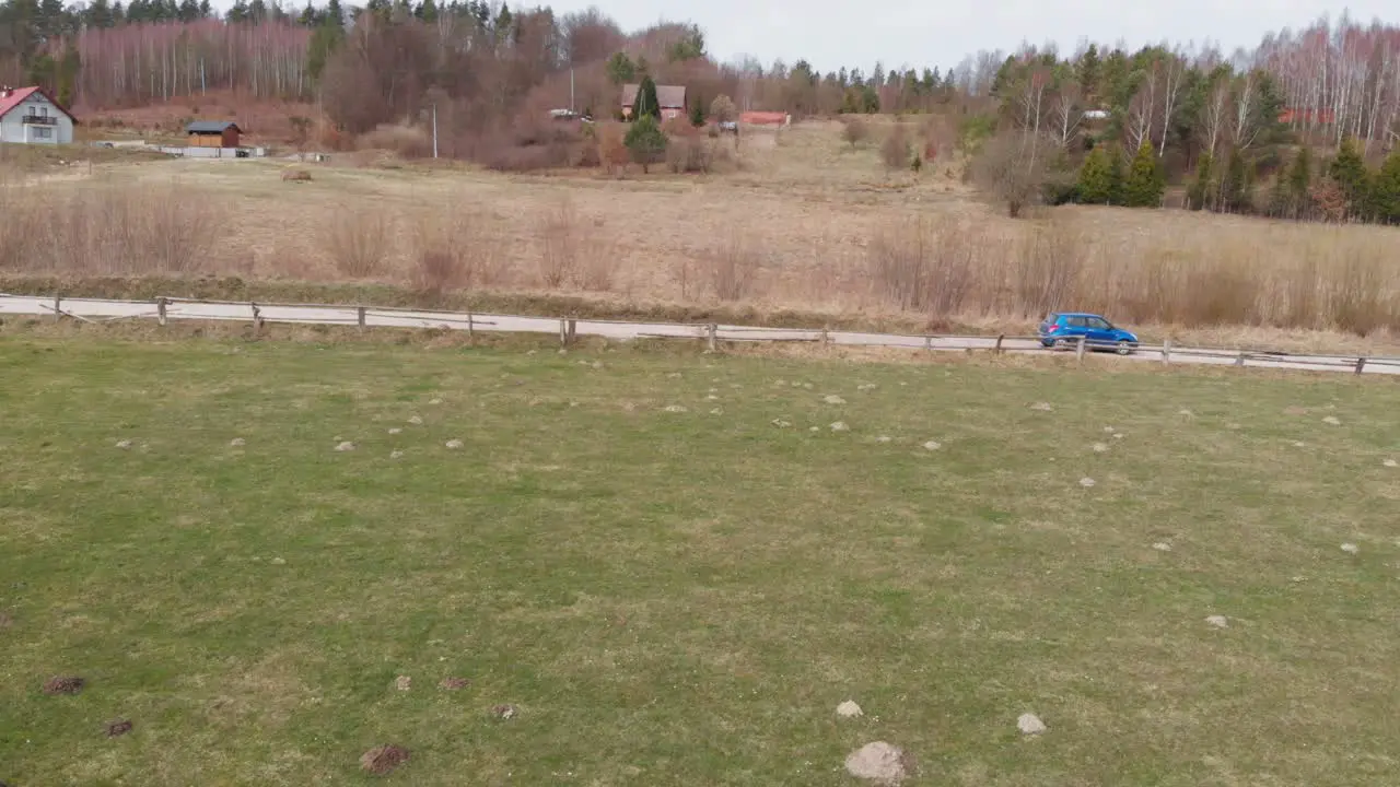 A blue car drives on a country road passing by two people