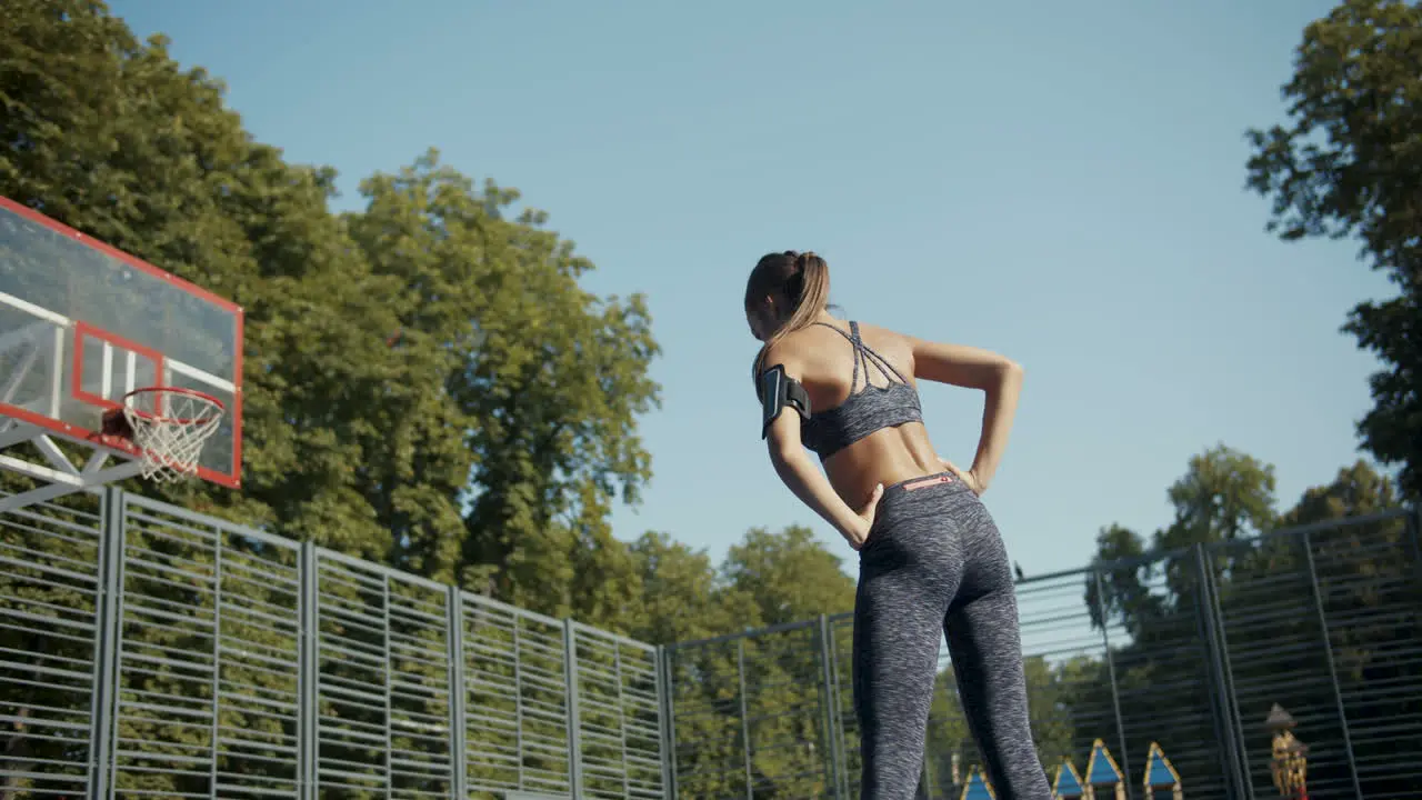 Rear View Of A Sporty Woman Warming Up And Stretching At Outdoor Basketball Court On A Summer Morning