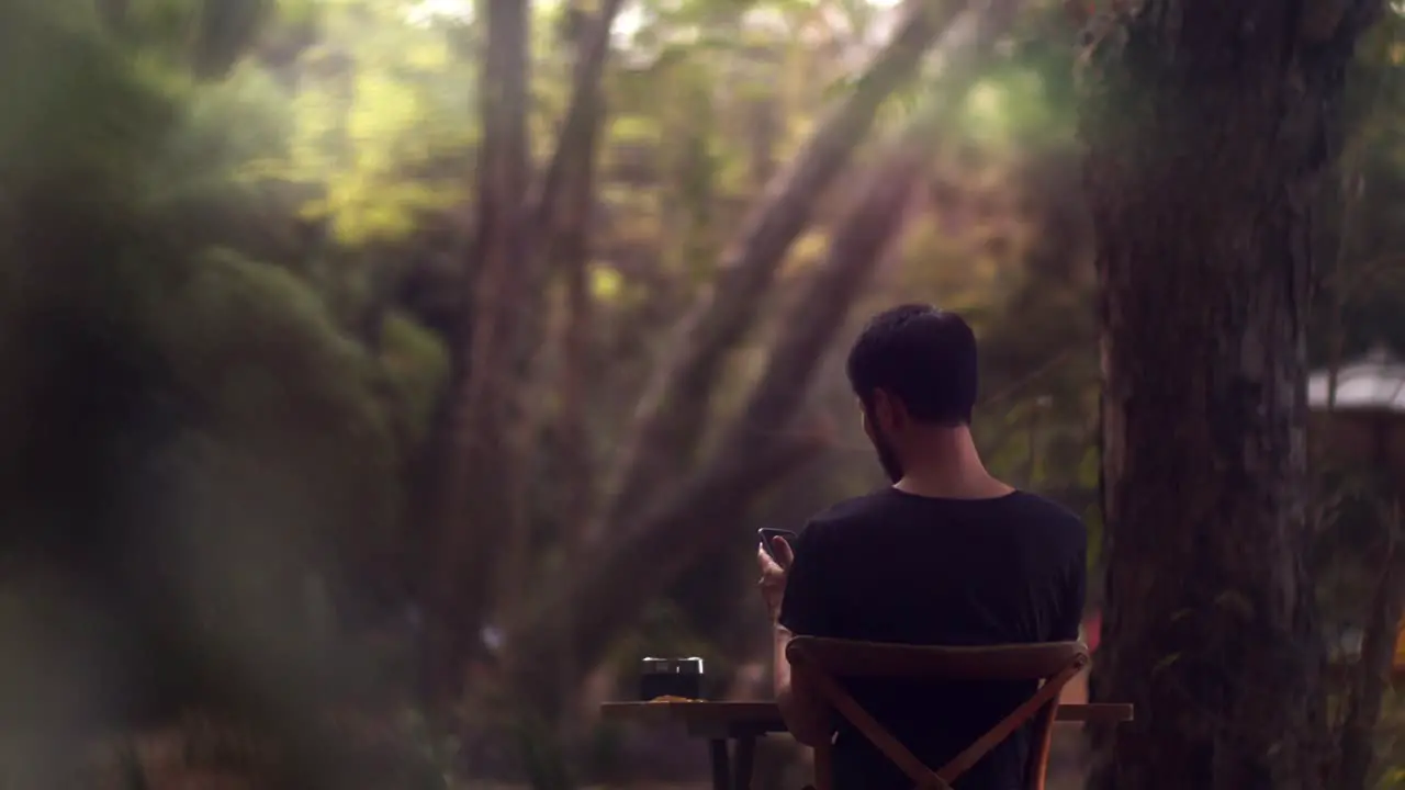 Asian man sitting outside in the garden at a table and working on his smartphone cinematic shot