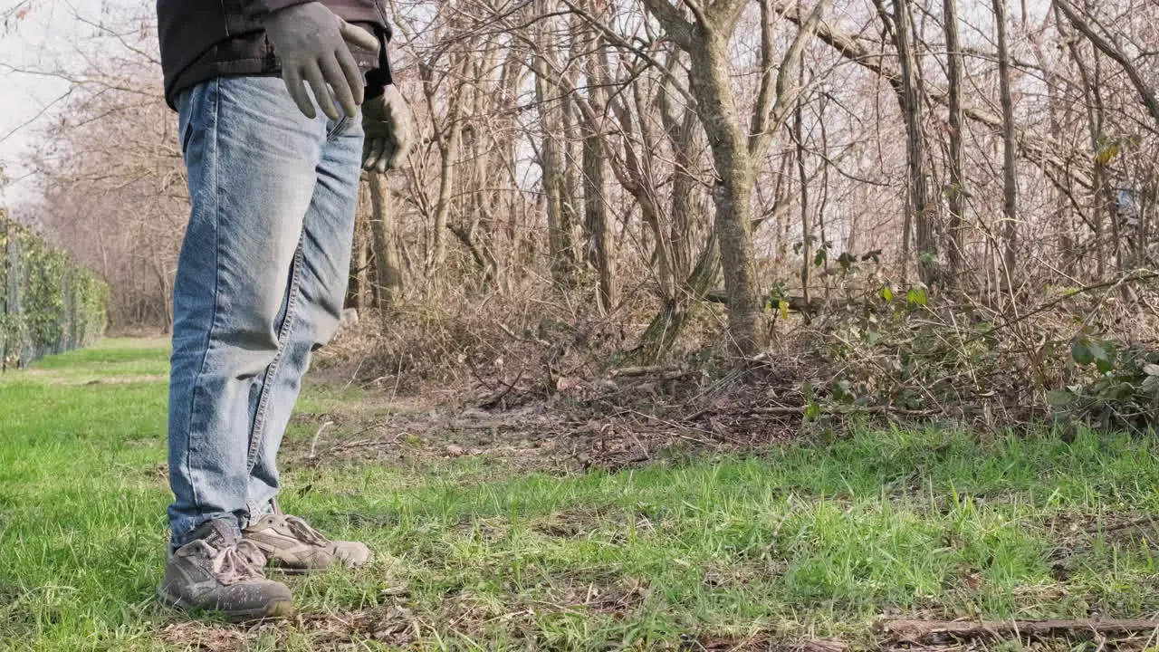 Man In Blue Jeans With Black Jacket And Gloves Standing In Front Of The Woods During Sunny Winter Day Static Close Up View