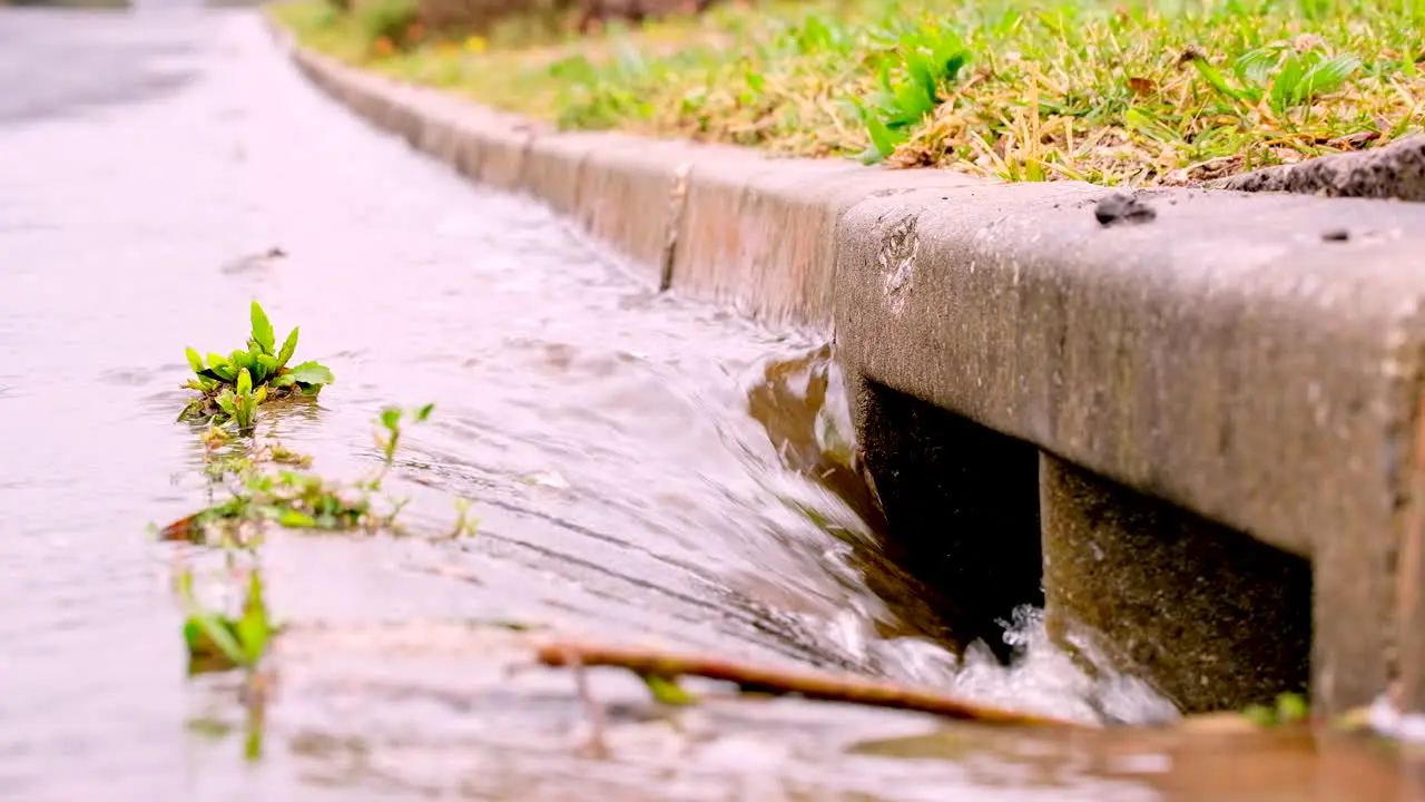 Rainwater runoff torrent runs down concrete gutter into stormwater road drain