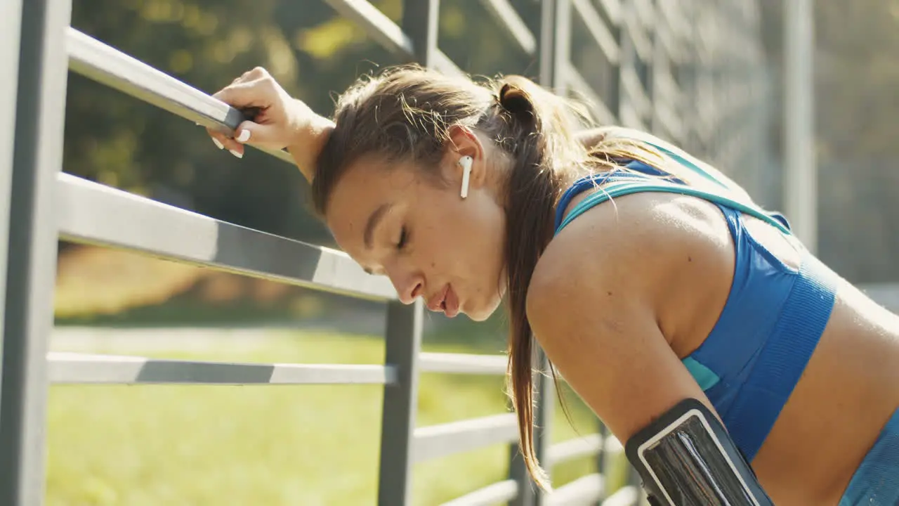 Side View Of A Tired Sportswoman With Airpods Resting And Breathing Hard After Workout At Outdoor Court On A Summer Day