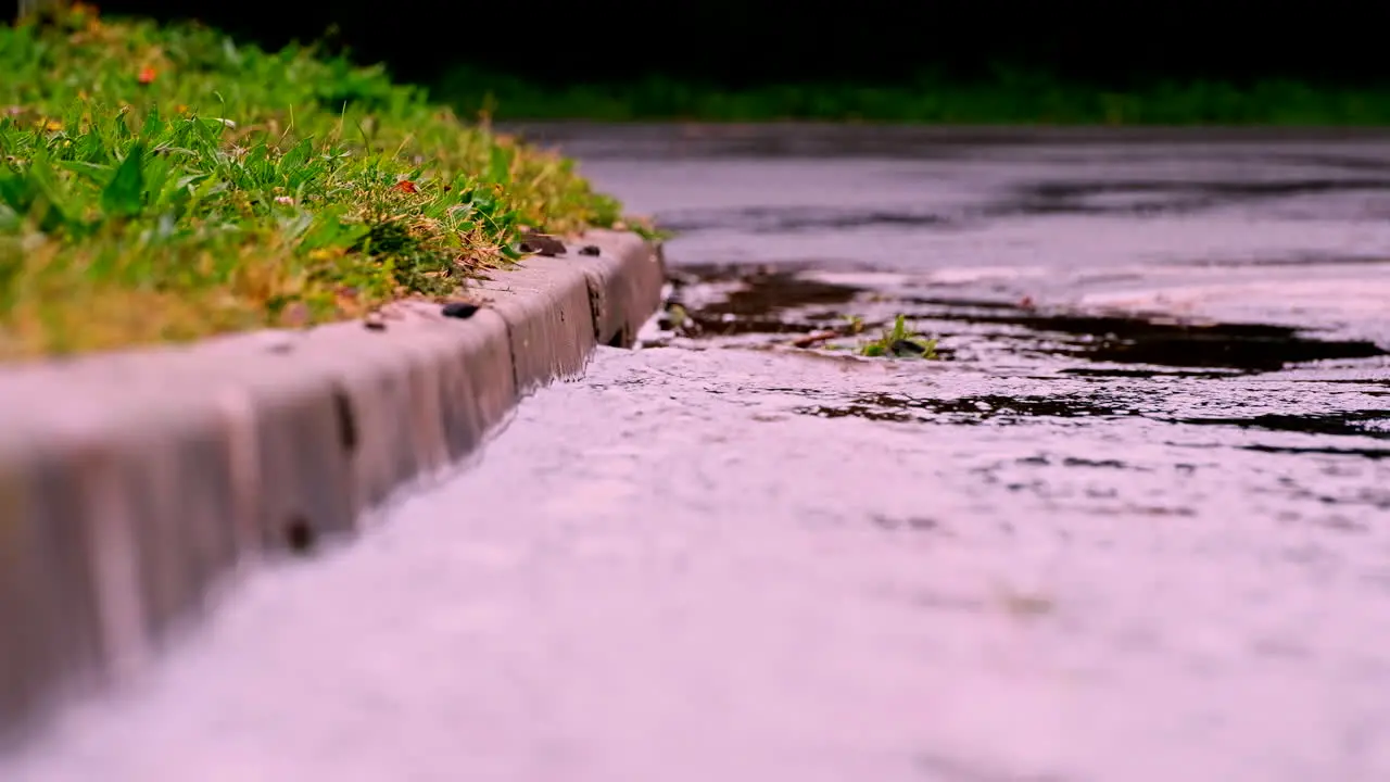 Rainwater runoff downhill towards concrete street drain telephoto shot