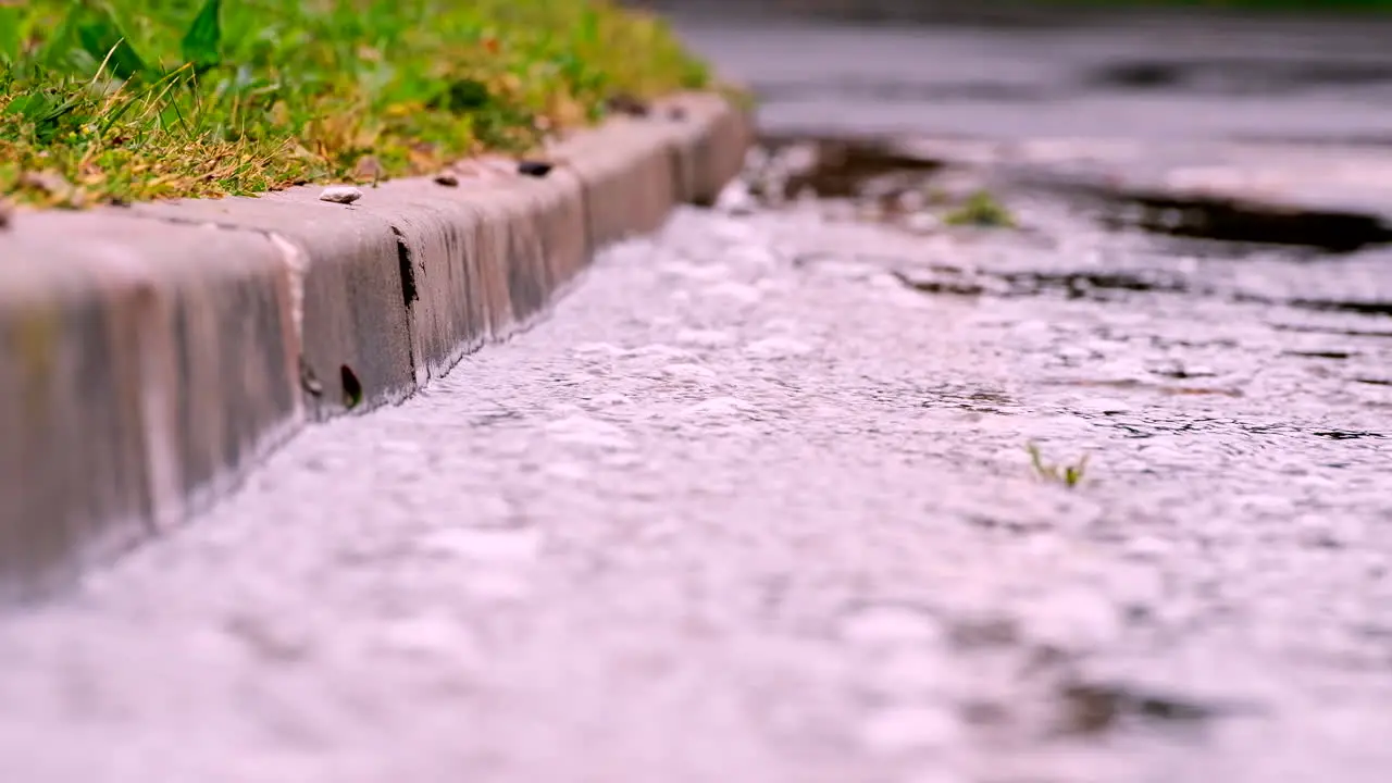 Rainwater runs down concrete gutter towards drain after heavy downpour