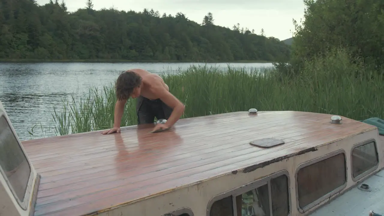 Fit young man topless sanding timber roof planking of old wooden boat