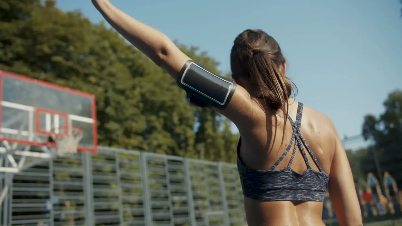 Rear View Of A Sporty Woman Warming Up Her Arm At Outdoor Basketball Court On A Sunny Morning