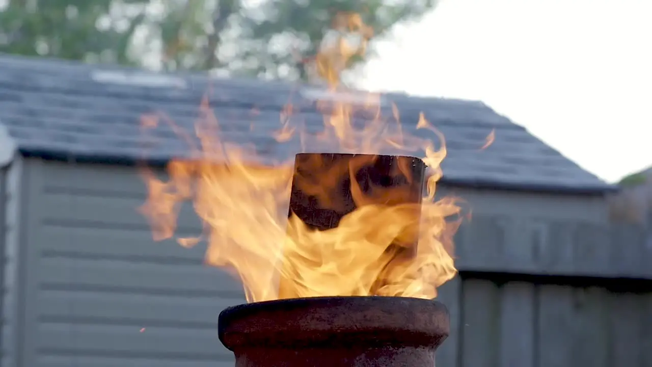 SLO-MO A low angle view of a board sticking out the top of a chimenea as flames rise up around it