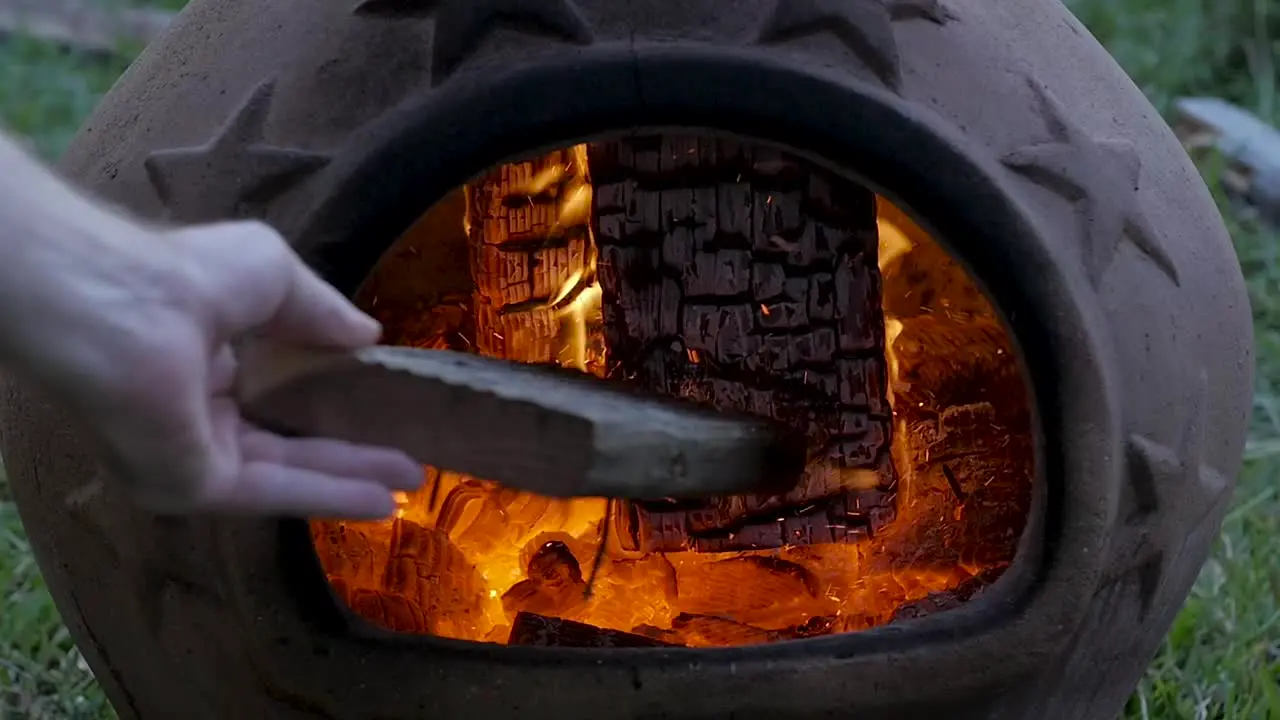 SLO-MO Caucasian male bumps burning embers in a terra-cotta chimenea with a piece of wood during late evening