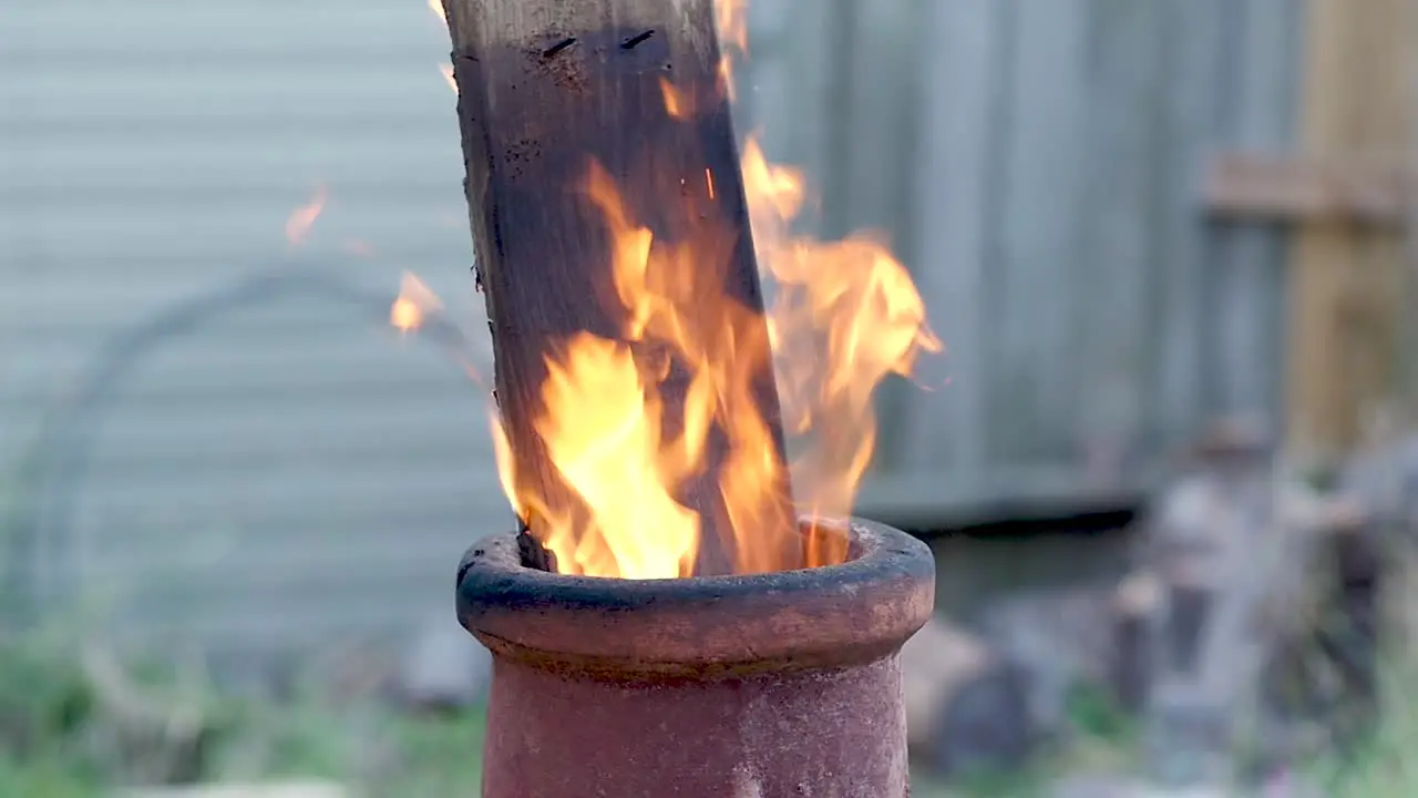 SLO-MO A board sticks out the top of a terra-cotta chimenea as flames rise around it during late evening