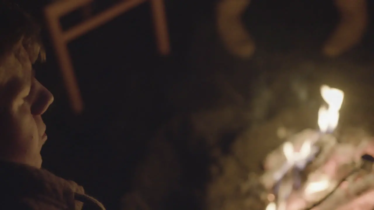 Young Male Traveler toasting smores with his friends at a bonfire