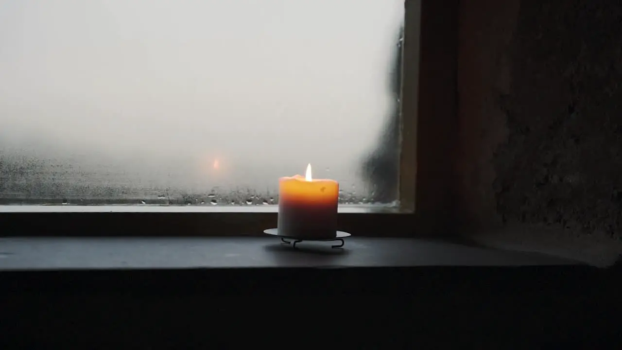 Candle flickering on window sill with rainy weather outside