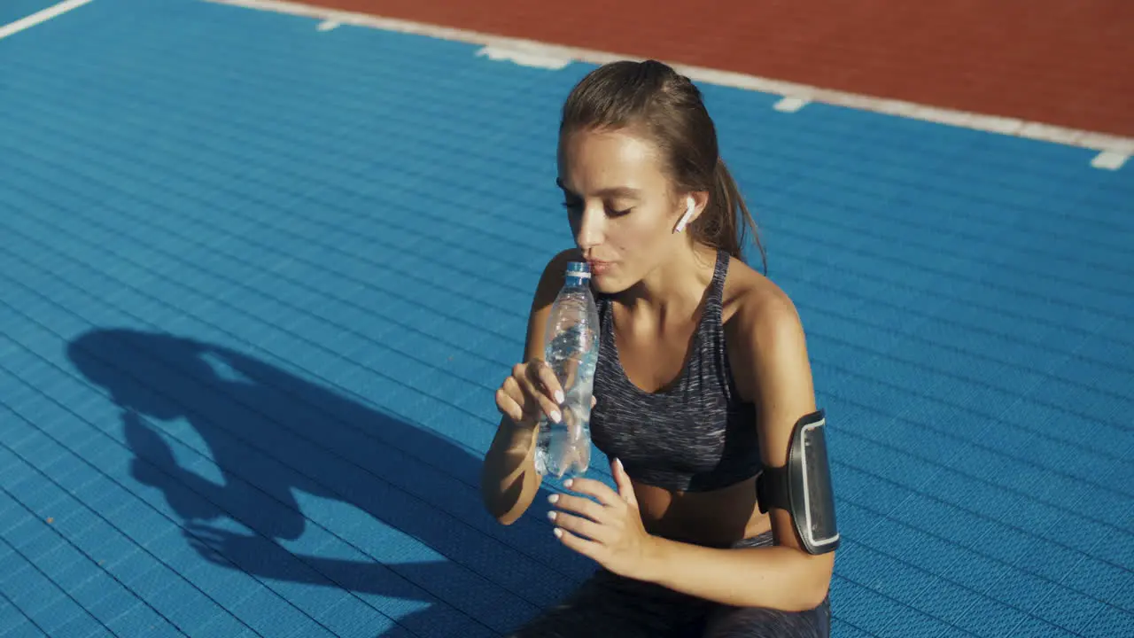 Fitness Woman Sitting At Sport Court And Drinking Cold Water After Workout On A Summer Day 1