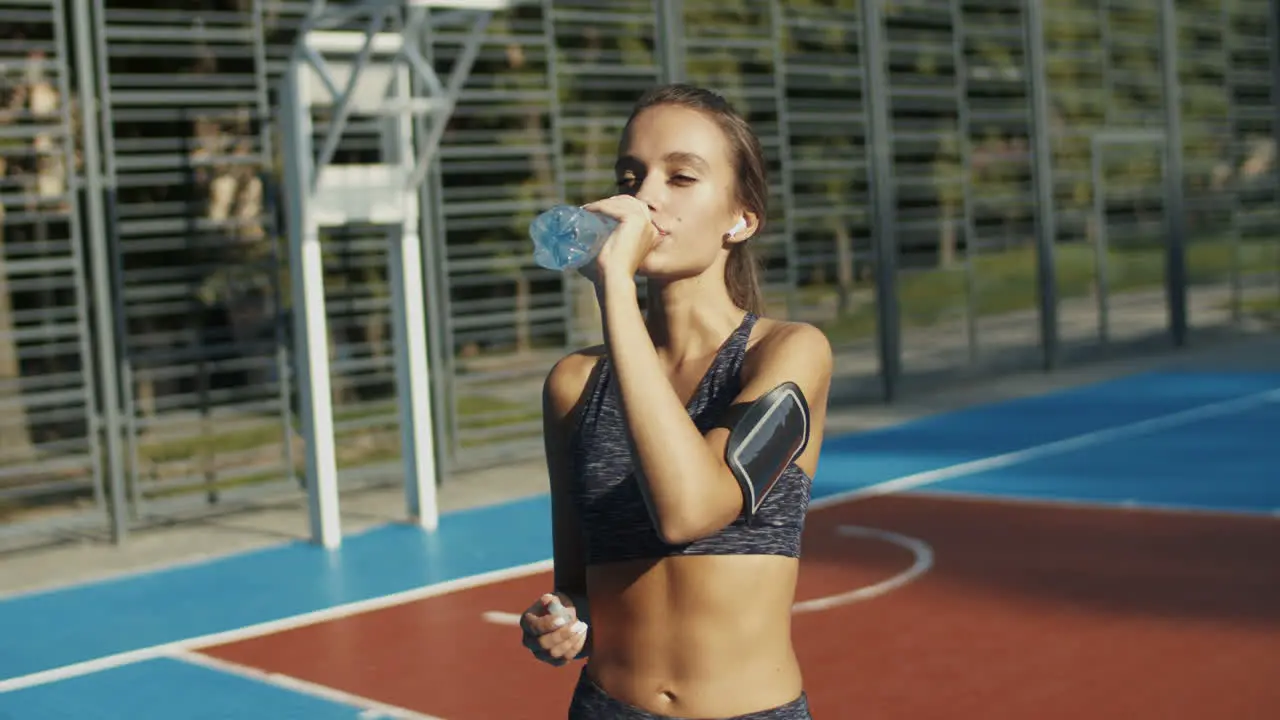 Sporty Woman Standing At An Outdoor Court Resting And Drinking Cold Water After Workout