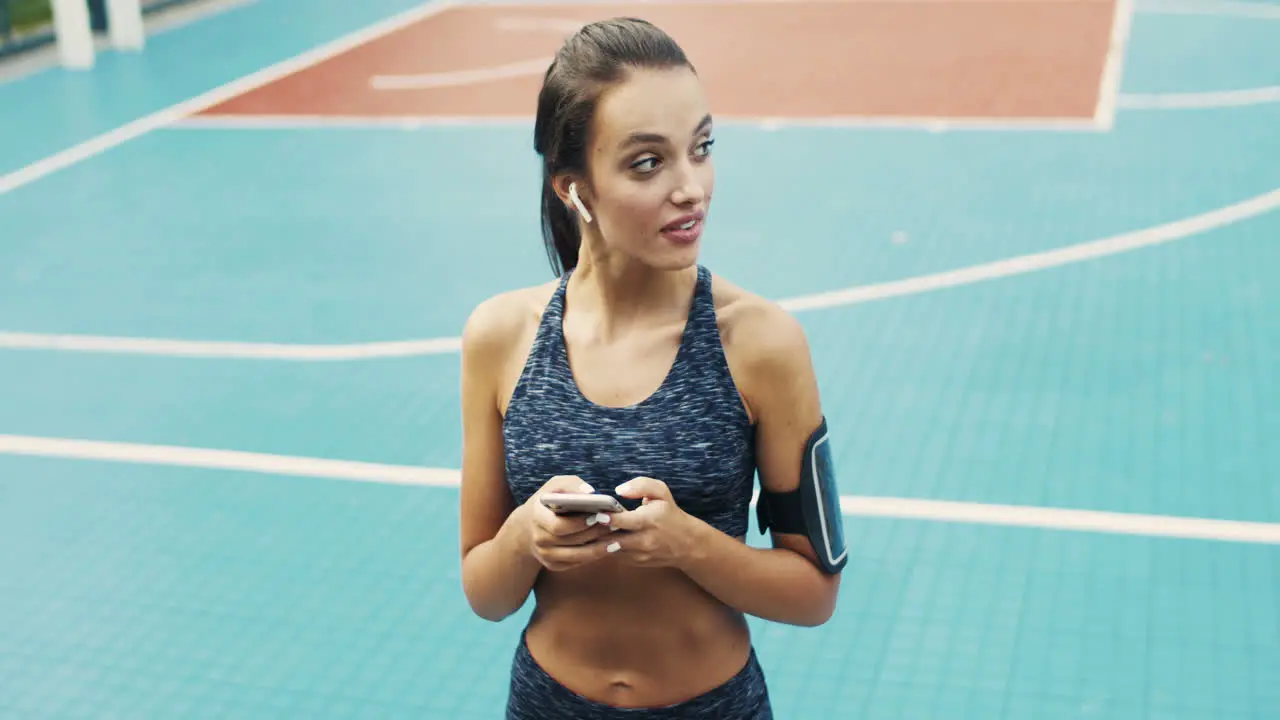 Sporty Girl With Airpods Texting Message On Smartphone While Standing At Outdoor Court On A Summer Day 1