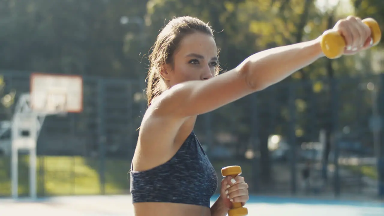 Sporty Girl Doing Dumbbell Punches Exercise At Outdoor Basketball Court In Summer Morning