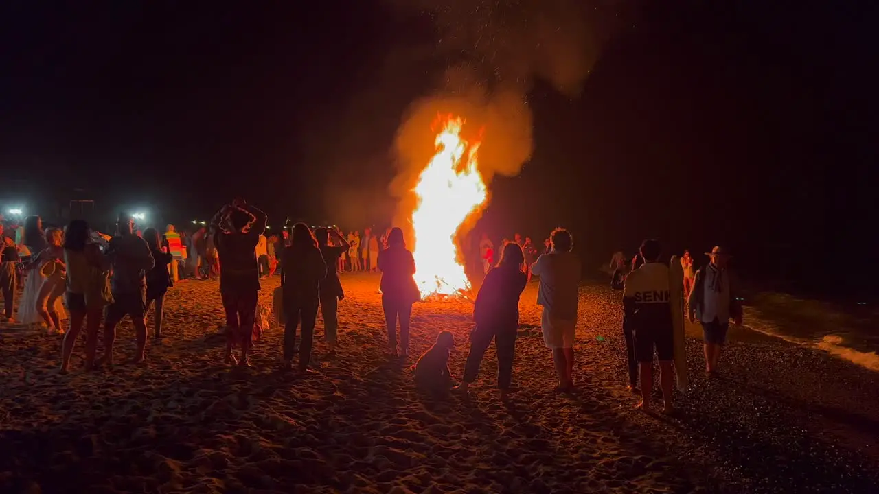 People dancing at traditional bonfire summer festival at the beach at the San Juan celebration in Marbella Spain enjoying a fun party big burning fire and hot flames at night 4K shot