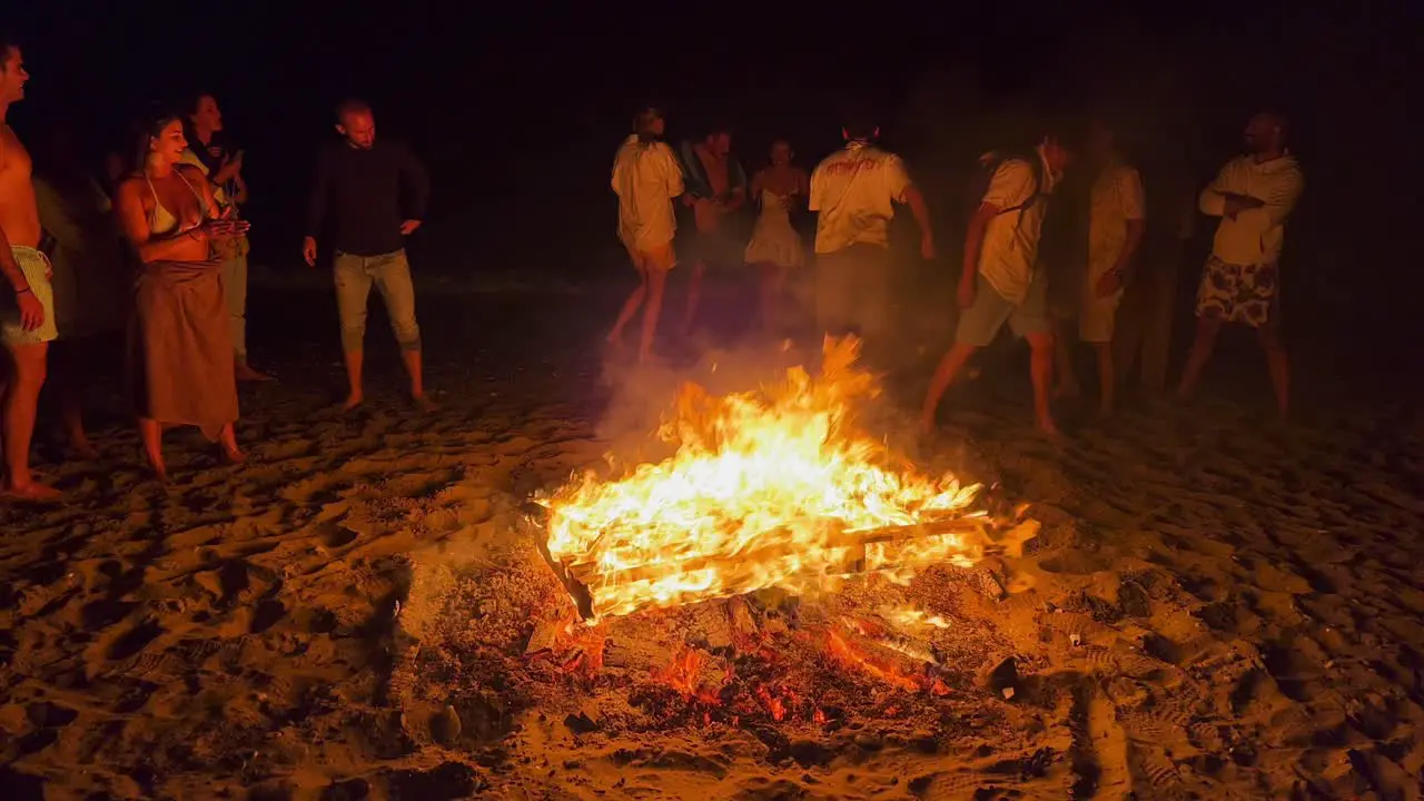 People jumping over a traditional bonfire at the San Juan festival at the beach in Marbella Spain friends and family enjoying a fun party jumping over a burning fire and hot flames at night 4K shot