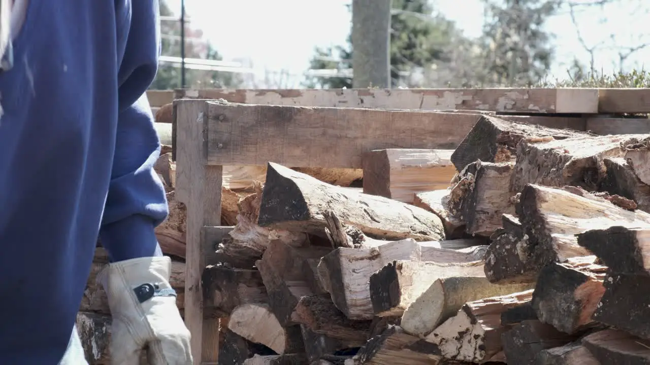 Man in blue shirt and work gloves stacks fire wood into a neat pile