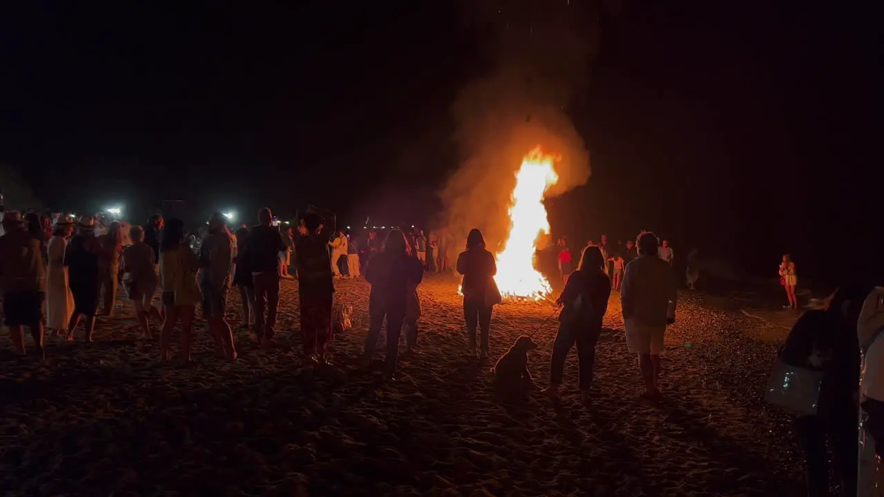 Big crowd at the traditional bonfire festival at the beach at the San Juan celebration in Marbella Spain friends and family enjoying a fun party during summer burning fire and hot flames 4K shot