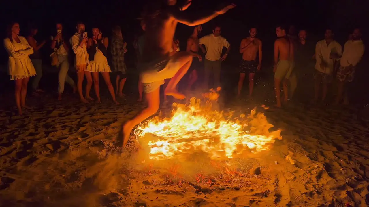 People jumping over a traditional bonfire at the San Juan festival at the beach in Marbella Spain friends and family enjoying a fun party jumping over a big burning fire and hot flames 4K shot