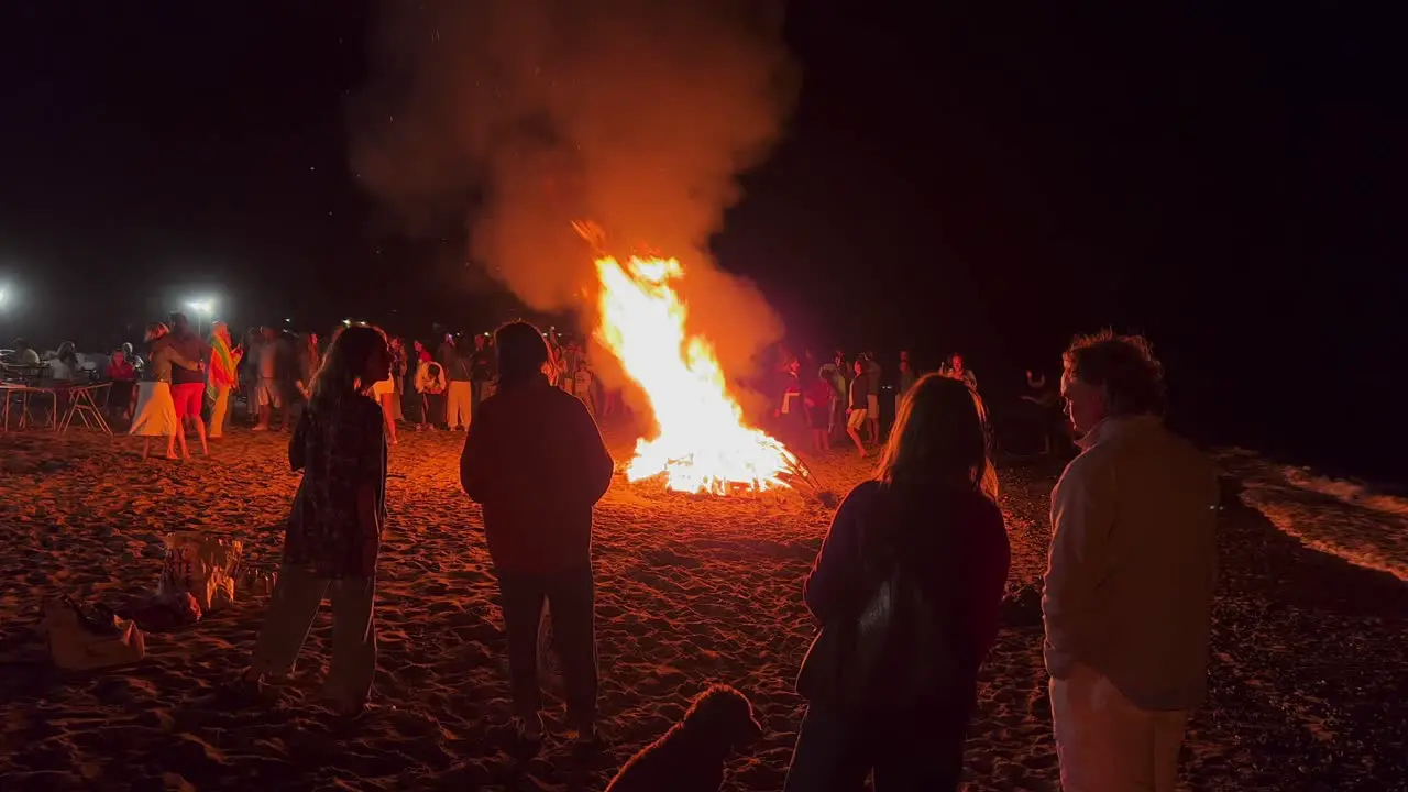 Big crowd at the traditional bonfire festival at the beach at the San Juan celebration in Marbella Spain people dancing and enjoying a fun party during summer big burning fire and flames 4K shot