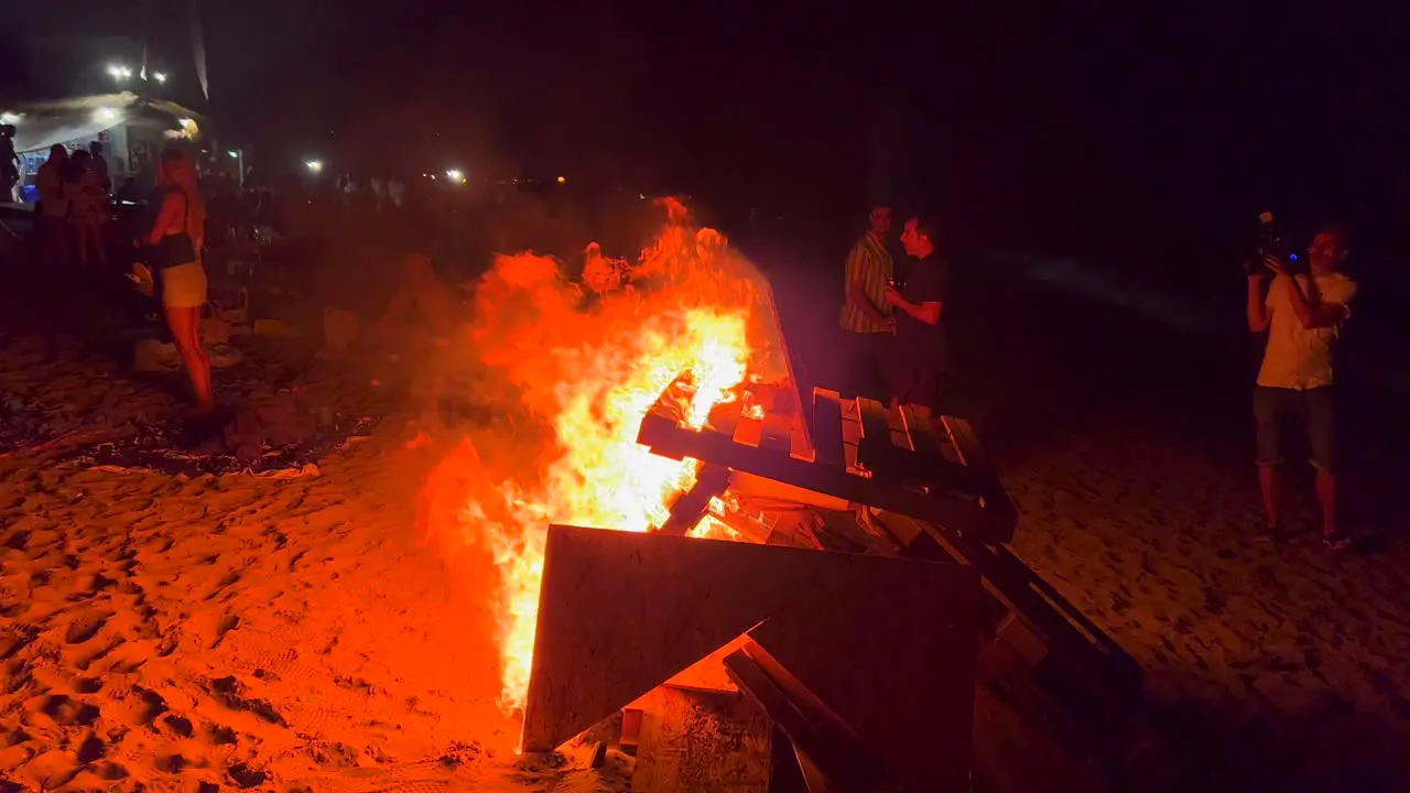 People at traditional bonfire summer festival at the beach at the San Juan celebration in Marbella Spain enjoying a fun party big burning fire and hot flames at night 4K shot