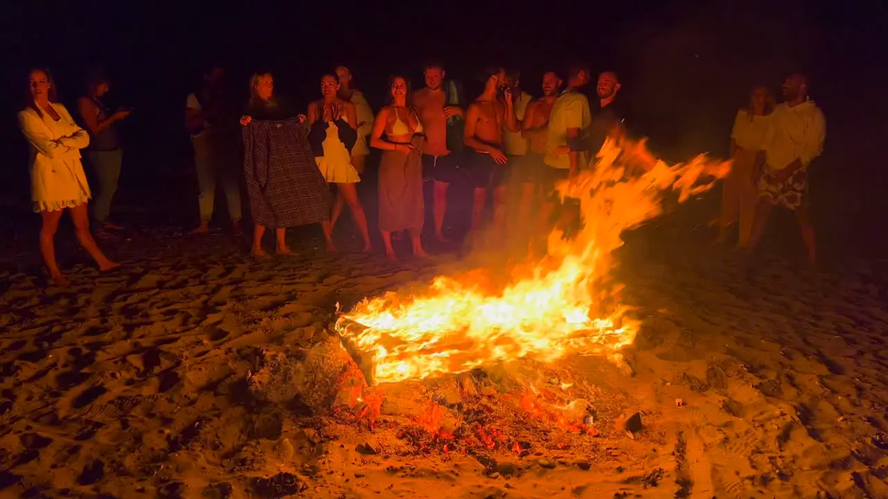 People jumping over traditional bonfire summer festival at the beach at the San Juan celebration in Marbella Spain enjoying a fun party big burning fire and hot flames at night 4K shot