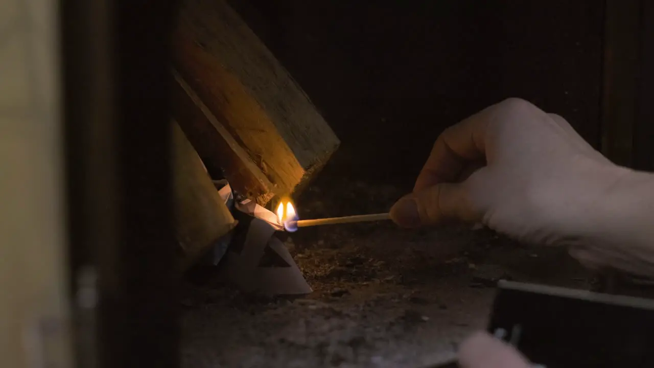 Close up of old elderly Caucasian woman lady grandma hands lighting a wooden match to light a cozy warm fire in a fireplace oven stove in a cabin during snowy cold Christmas xmas celebration warmth