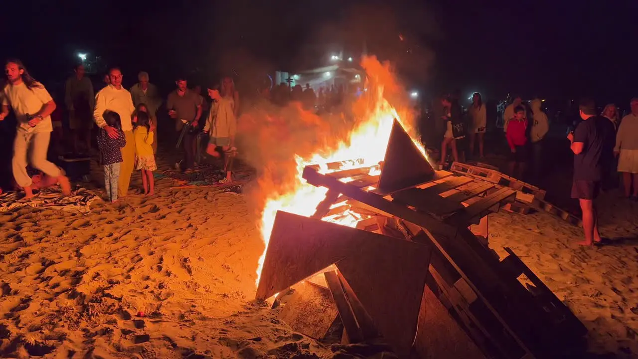 Traditional bonfire festival at the beach at the San Juan celebration in Marbella Spain friends and family enjoying a fun party during summer big burning fire and hot flames at night 4K shot