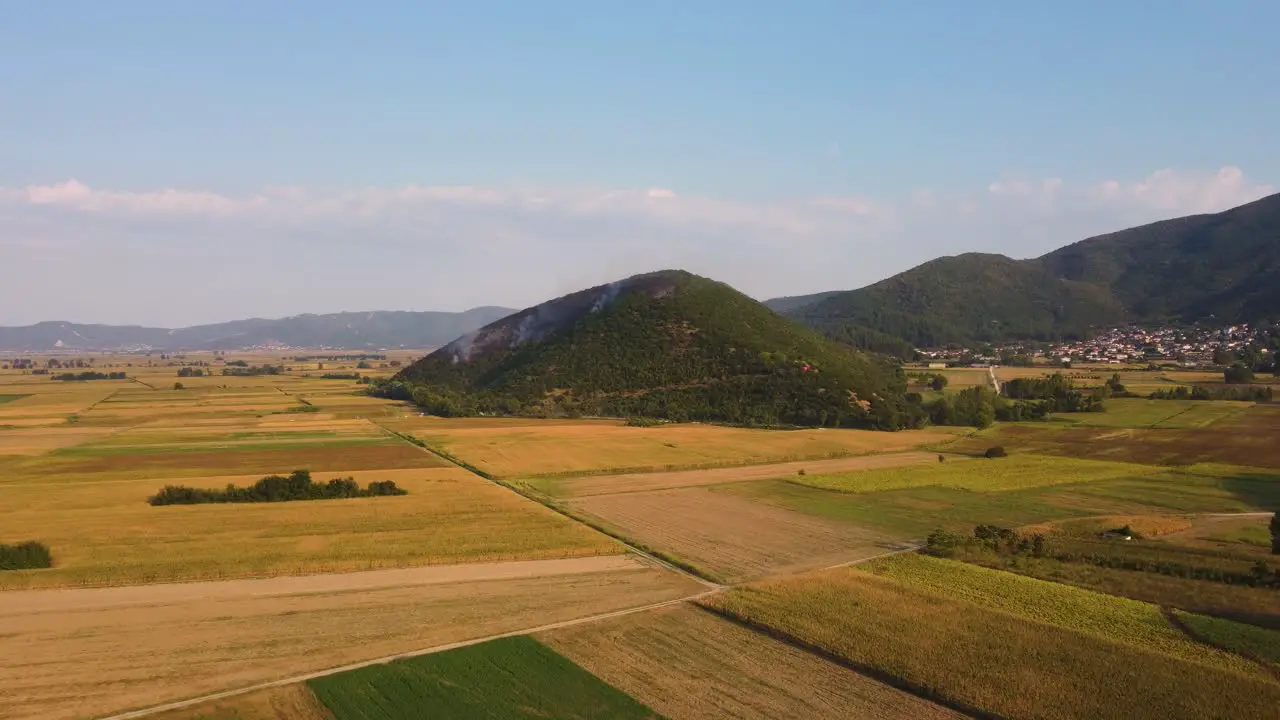 Establishing aerial shot of wildfire on a hill above agricultural fields in Greece