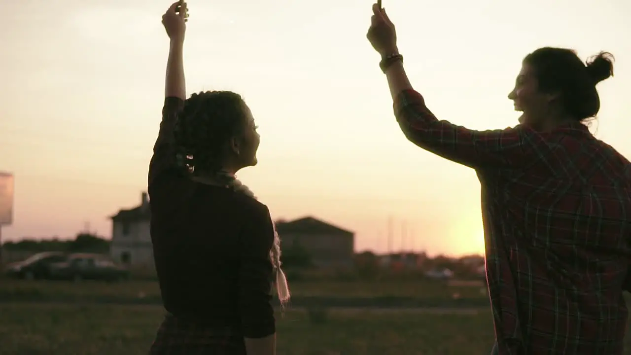 Back View Of Smiling Friends Having Fun Waving With Firework Candles During Sunset