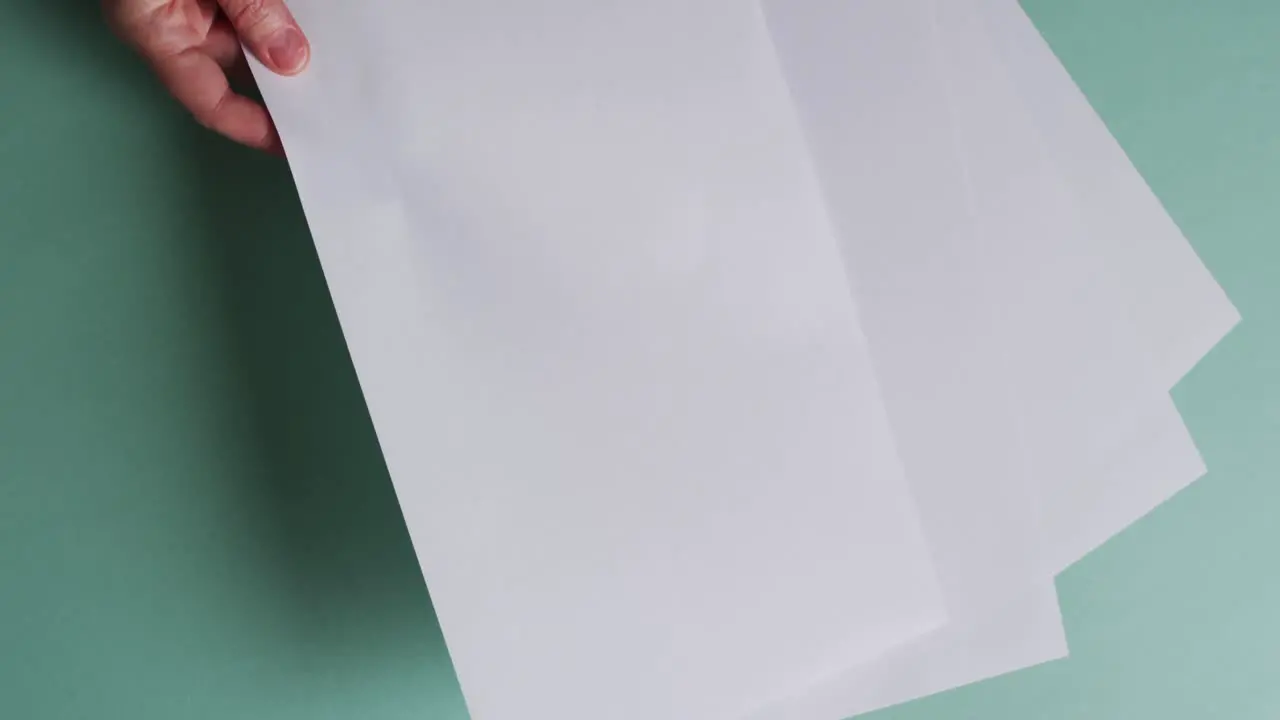 Hand holding piece of paper over pieces of paper with copy space on green background in slow motion