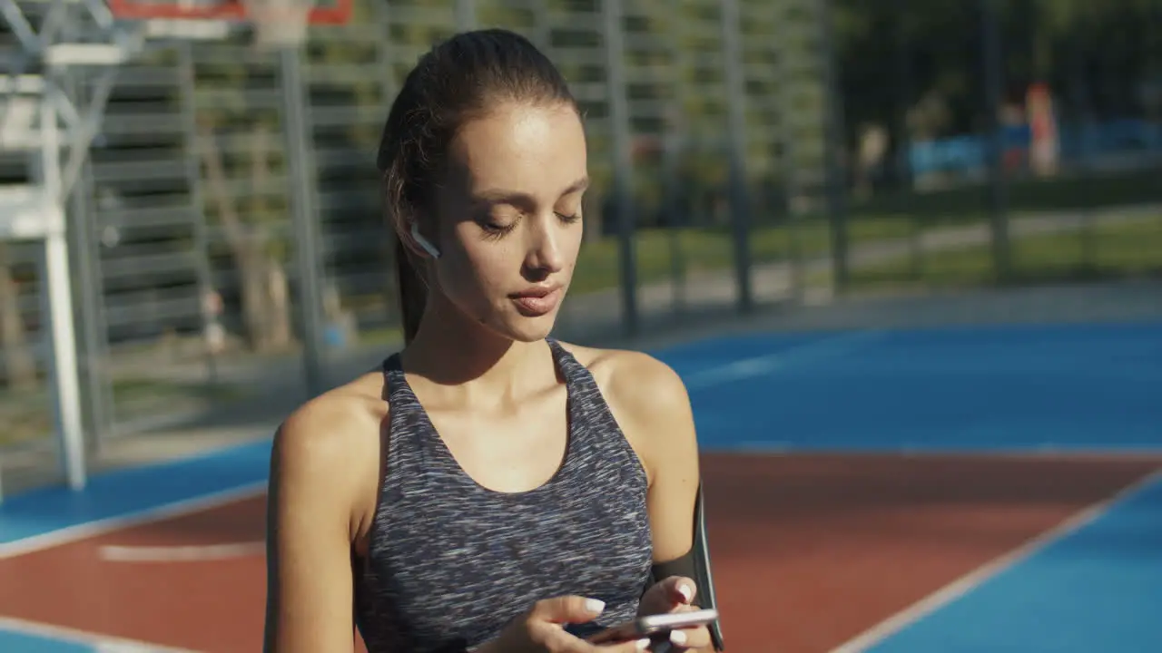 Sporty Girl With Airpods Laughing While Texting Message On Smartphone At Outdoor Court On A Summer Day 1