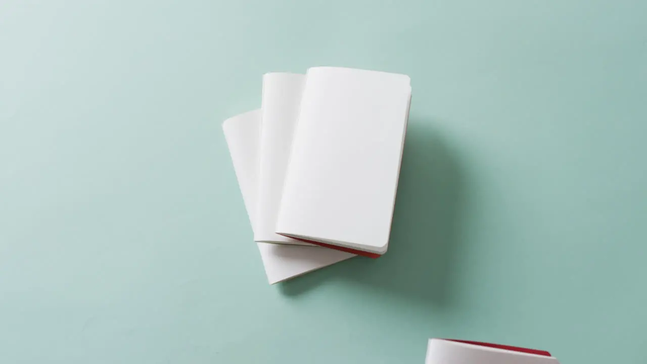 Hand keeping a notebook on stack of notebooks with copy space on green background in slow motion