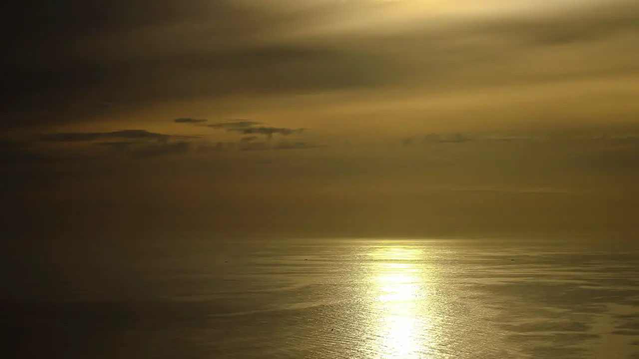 Golden reflections on sea surface and clouds moving in yellow sky