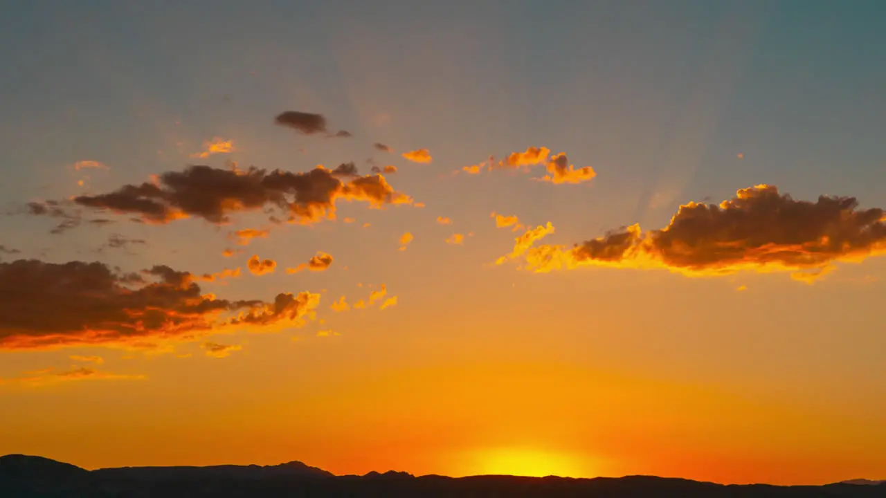 The sun sets behind the mountains in golden splendor as another day comes to an end static time lapse with