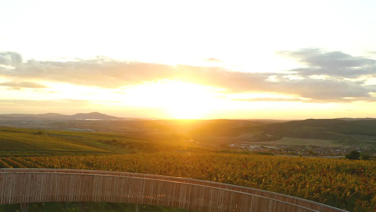 Lookout point Kobylí Vrch during sunset overlooking the wooden construction of the building in the background of the sun and rays with farms with vines and moving clouds area of South Moravia