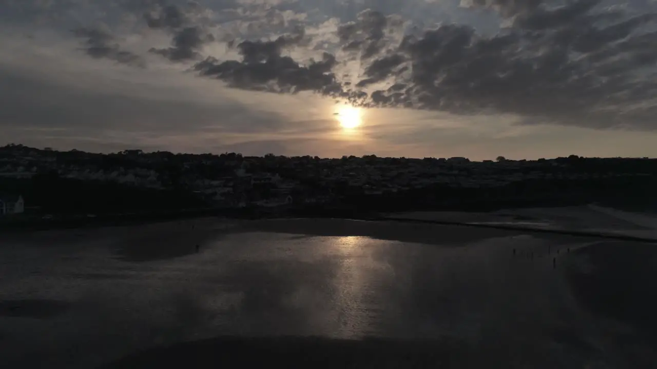 Evening cloudy golden sunset colours across Benllech beach silhouette coastline Anglesey aerial slow lowering view