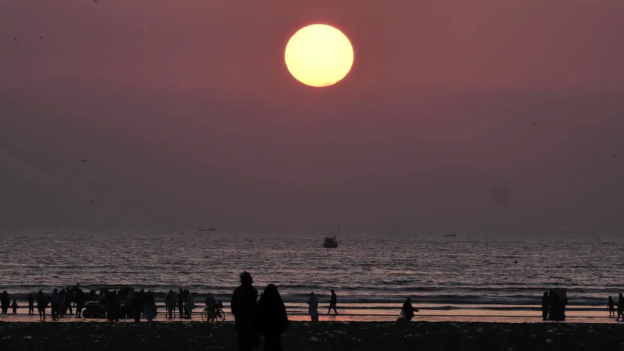 Yellow Sun With Sunset And Silhouette Of People On Karachi Beach Walking In Distance