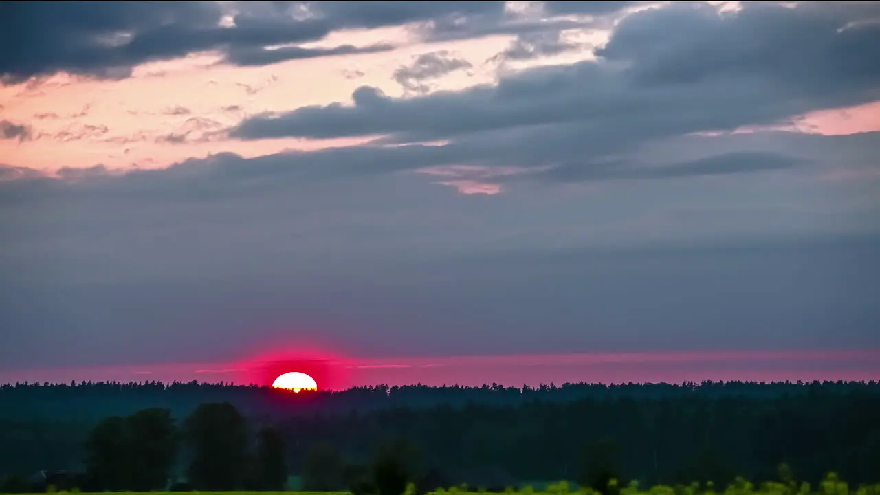 Pink sunset as the sun dips below the forest on the horizon during a dramatic cloudscape time lapse