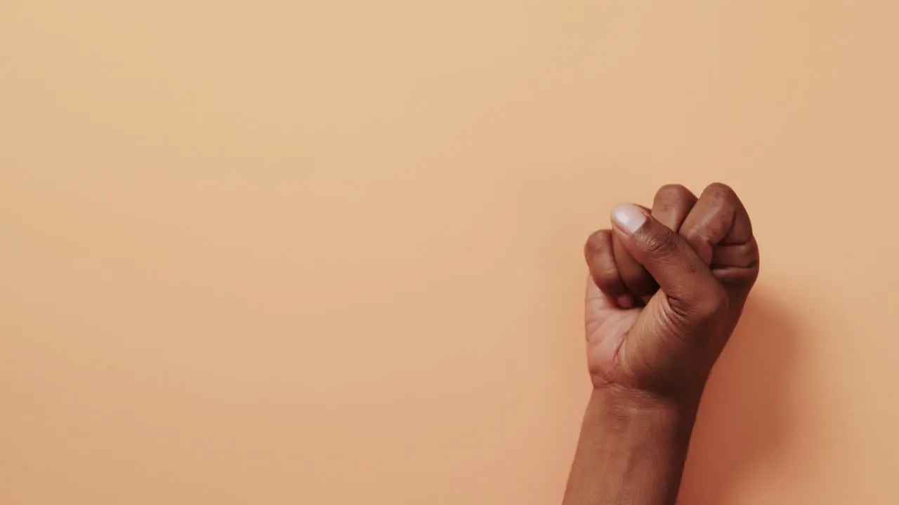 Close up of hand of biracial man showing peace sign with copy space on orange background