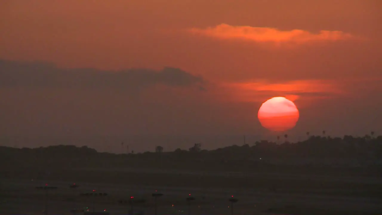 An orange ball of sun sets behind the LA hills