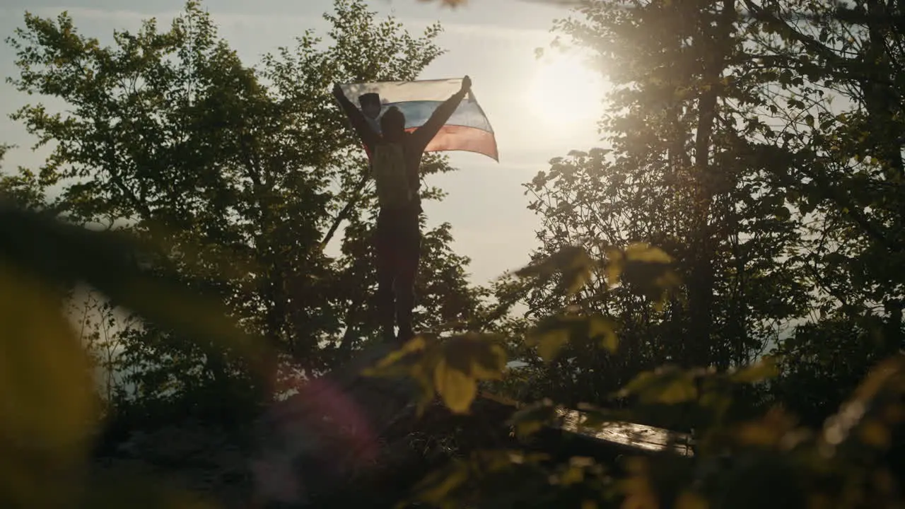 Frog's eye perspectice on man holding Slovenian flag towards the morning sun on peak of mountain Slivnica between the trees