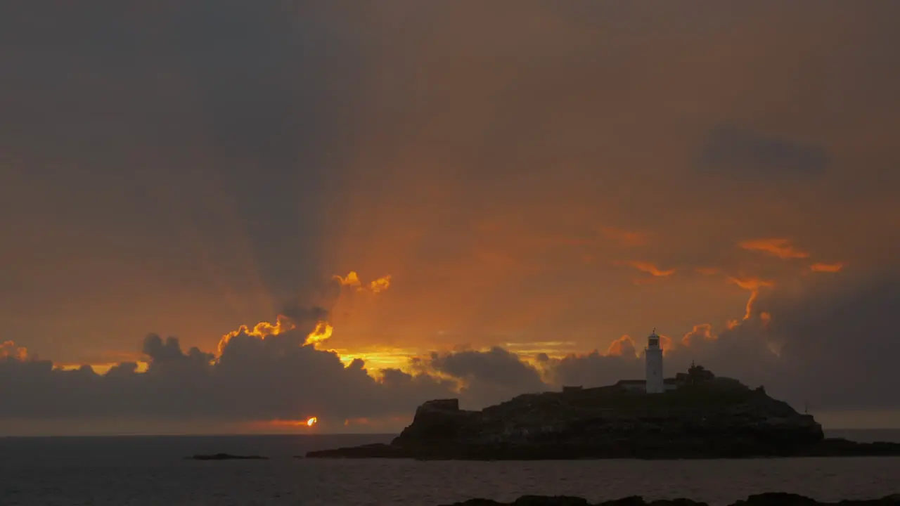 The beautiful sunbeams of the sun setting behind indigo clouds by the Godrevy Lighthouse in Cornwall England Wide shot