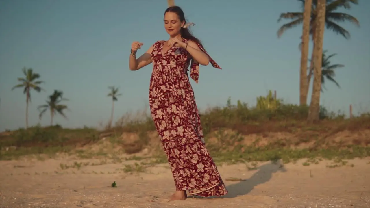 Woman taking deep breaths as she meditates while standing at the beach in a dress with trees behind her