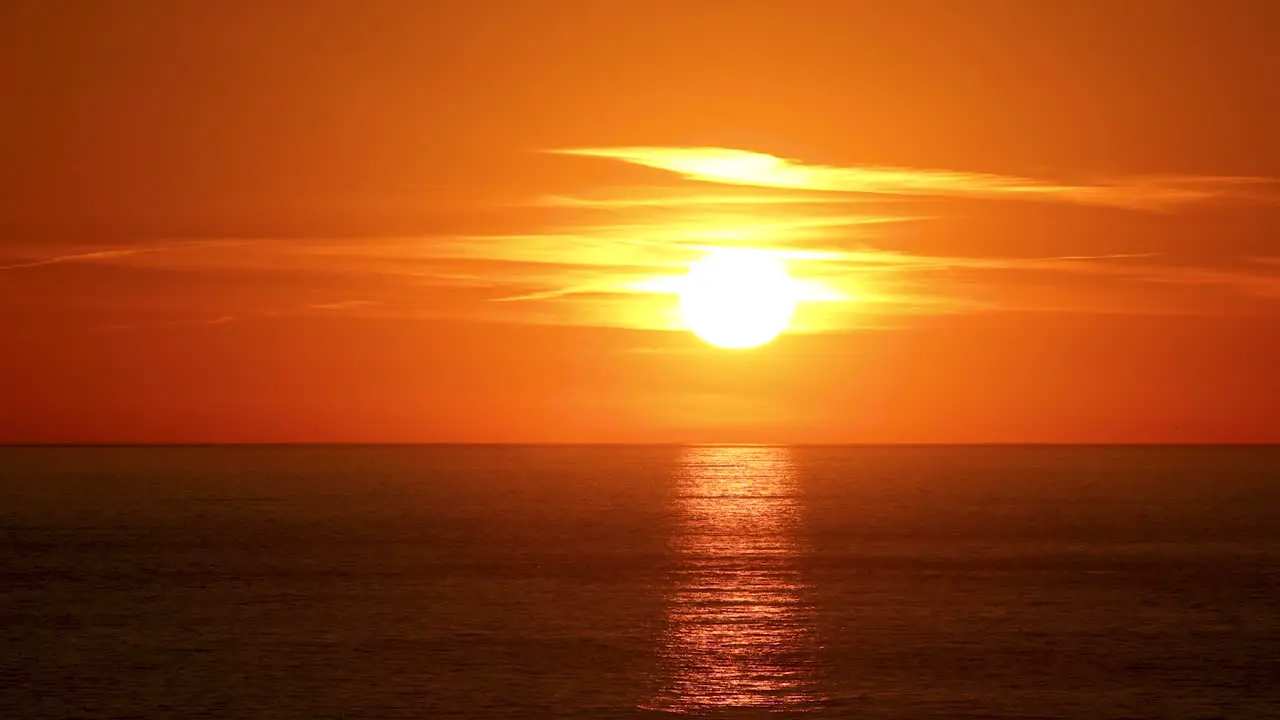 Beautiful sun behind dramatic orange clouds in sunset sky over ocean