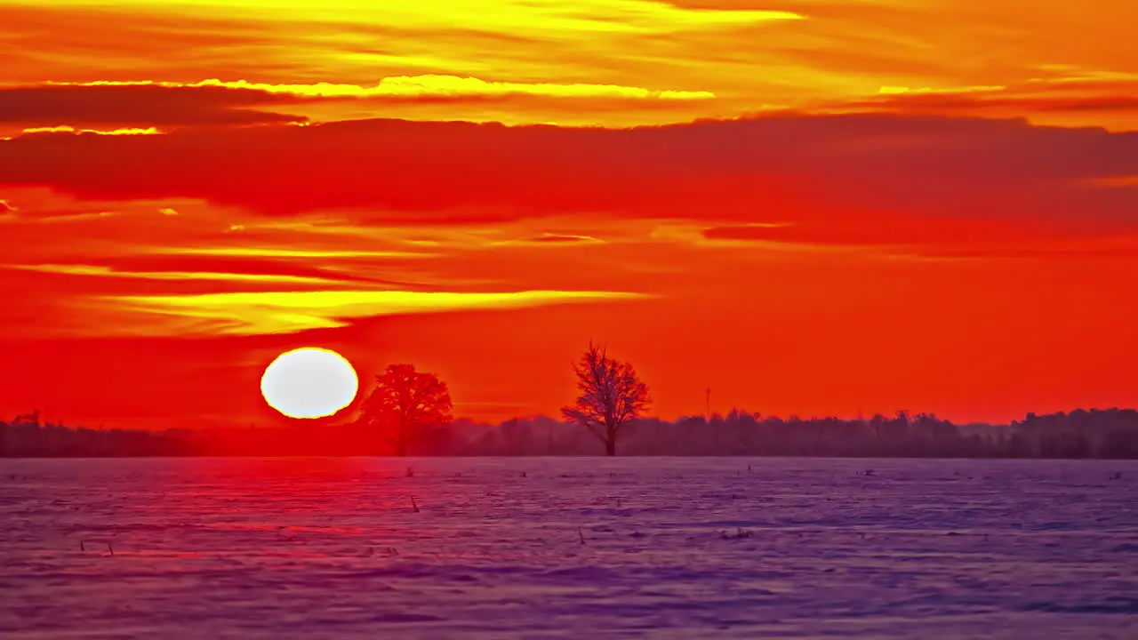 Bright colorful orange and crimson sunrise over snow on a winter farmland field time lapse