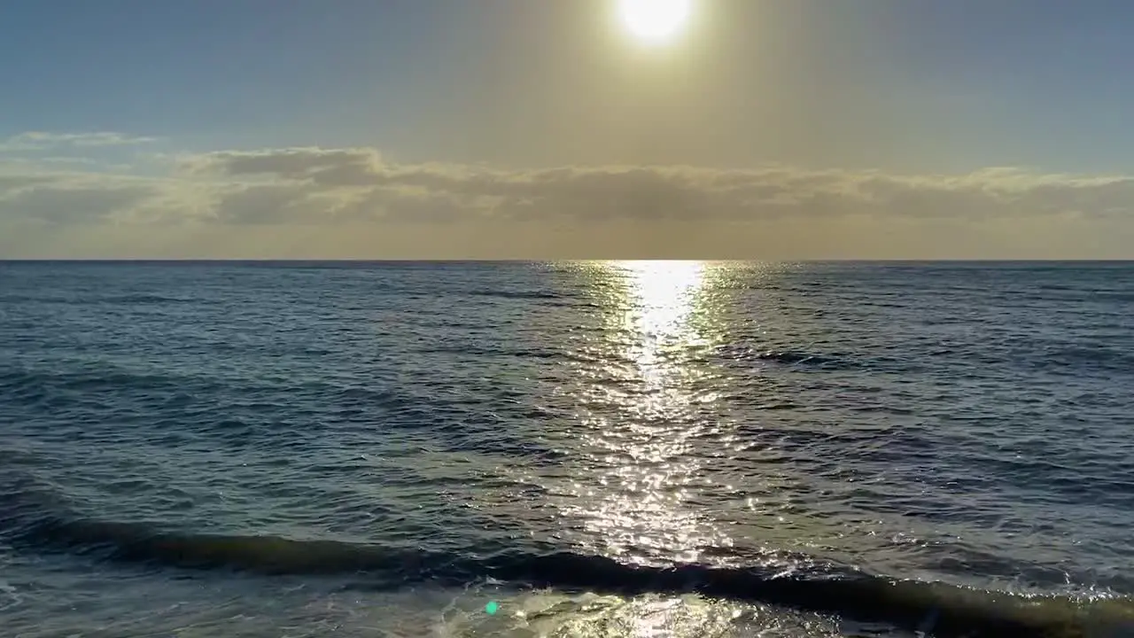 Slow tilt up from the gentle lapping waves of a deserted tropical beach at sunset towards the clear horizon as the sun descends and the sky turns yellow