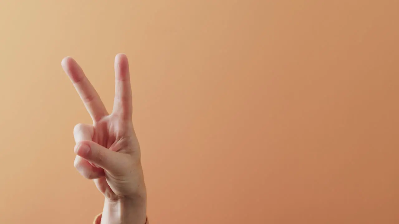 Close up of hand of cacausian woman showing peace sign with copy space on orange background