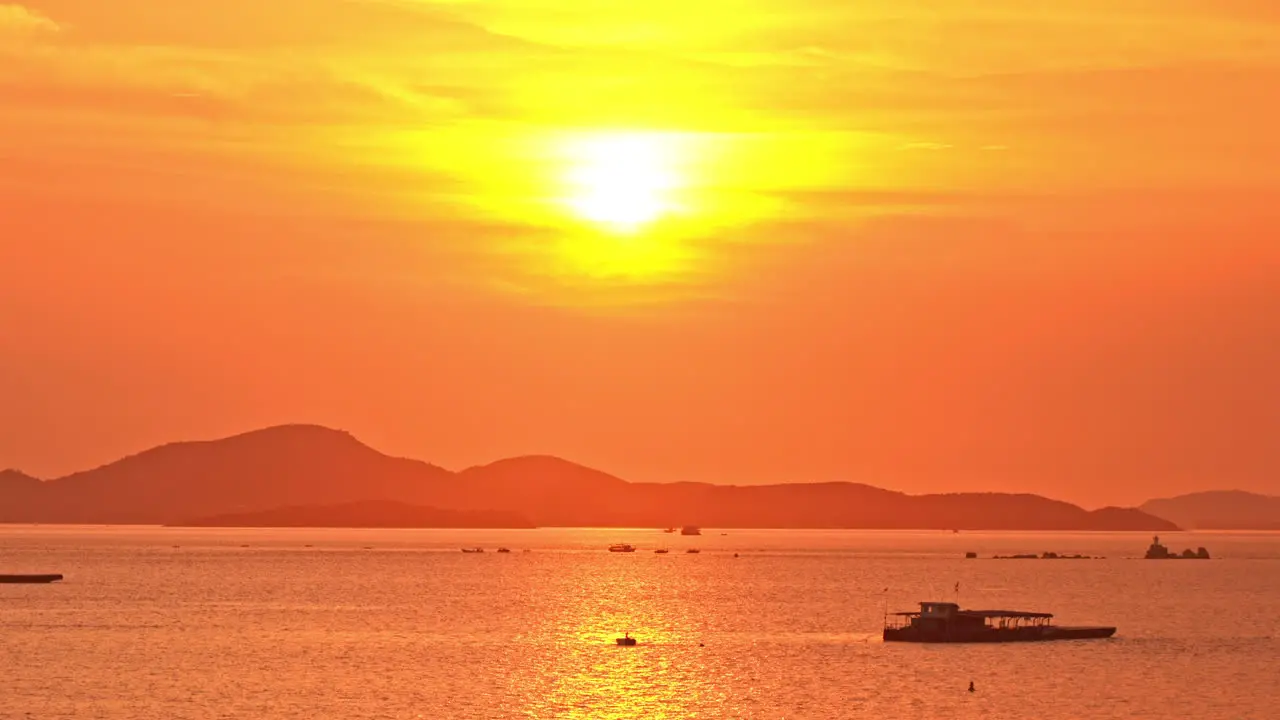 Tropical orange sunset reflecting on the water with hills and fishing boats